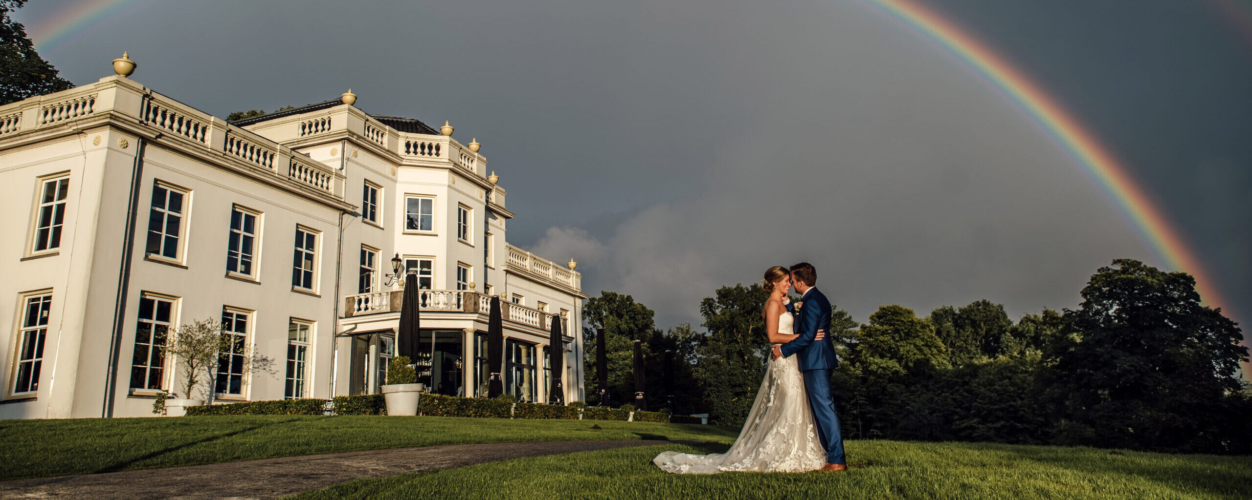 bruidspaar kust onder een regenboog voor stadsvilla sonsbeek, buiten trouwen, stadsvilla trouwen, arnhem, witte villa, huwelijk