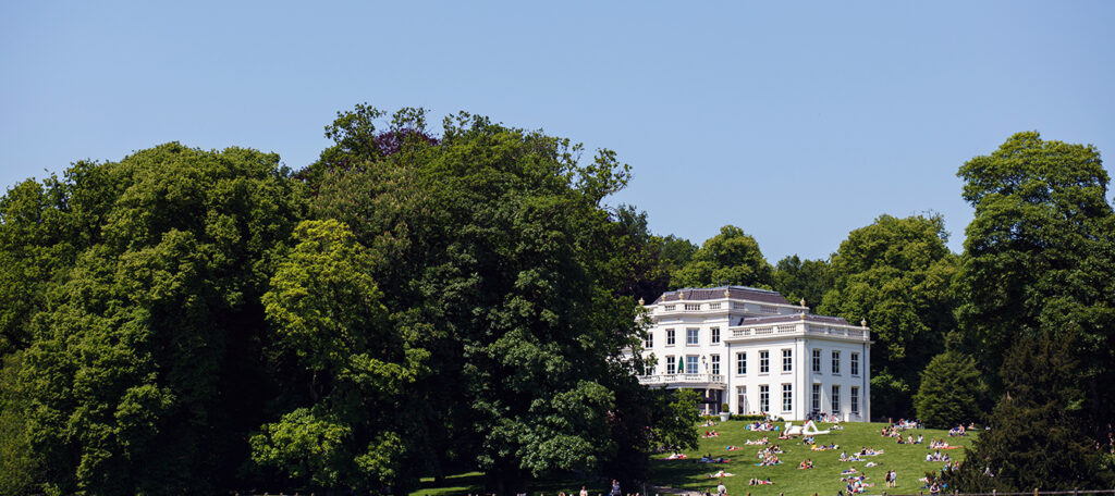 De witte stadsvillla sonsbeek, van ver af, op de heuvel, met een strakblauwe lucht